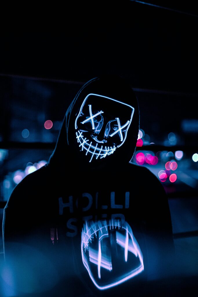 A person wearing a glowing neon mask with a hoodie in an urban night setting, Dominican Republic.